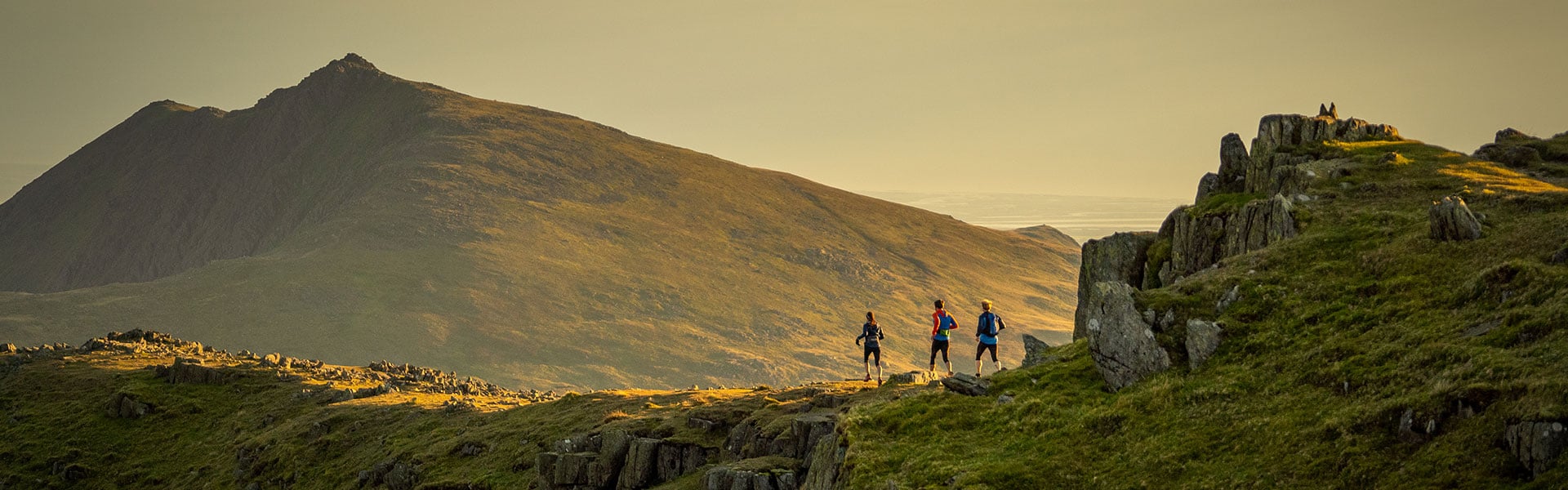Runners below a mountain ridge in evening light.