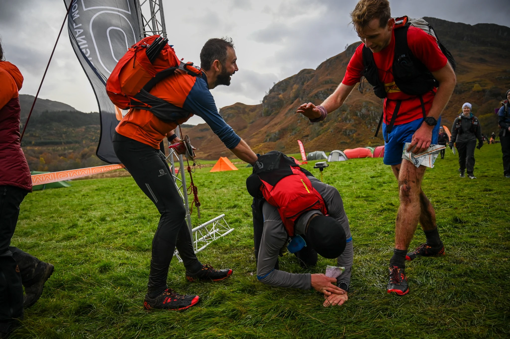 OMM competitors descending a grassy mountainside beneath steep crags