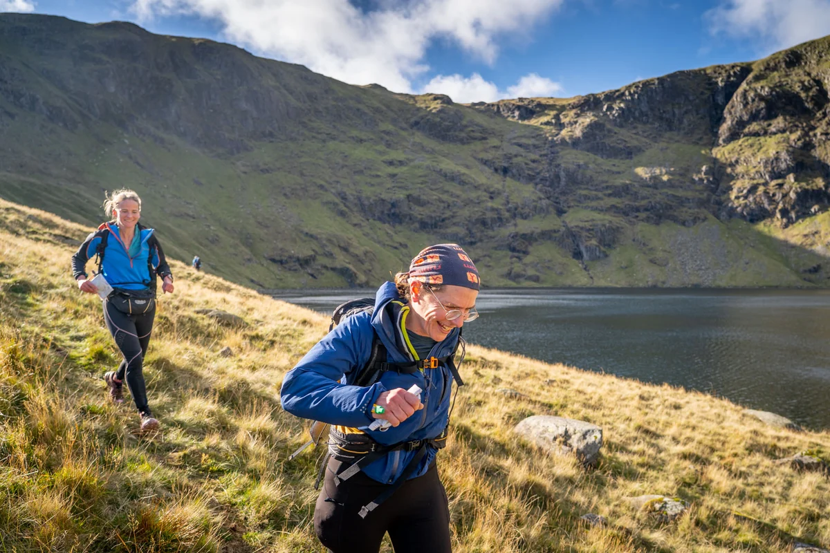 Competitor carrying a pack beside a mountain lake