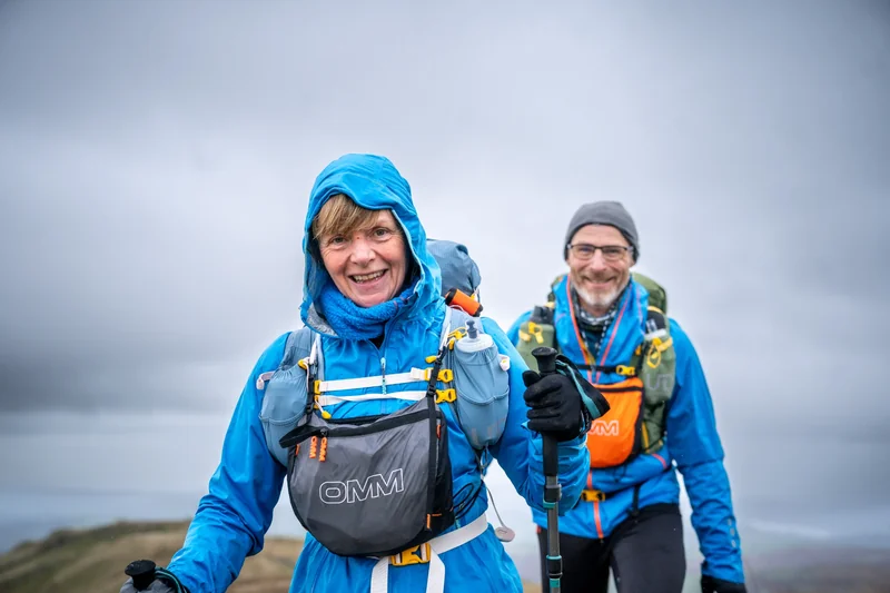 An OMM competitor carrying a pack beside a mountain lake