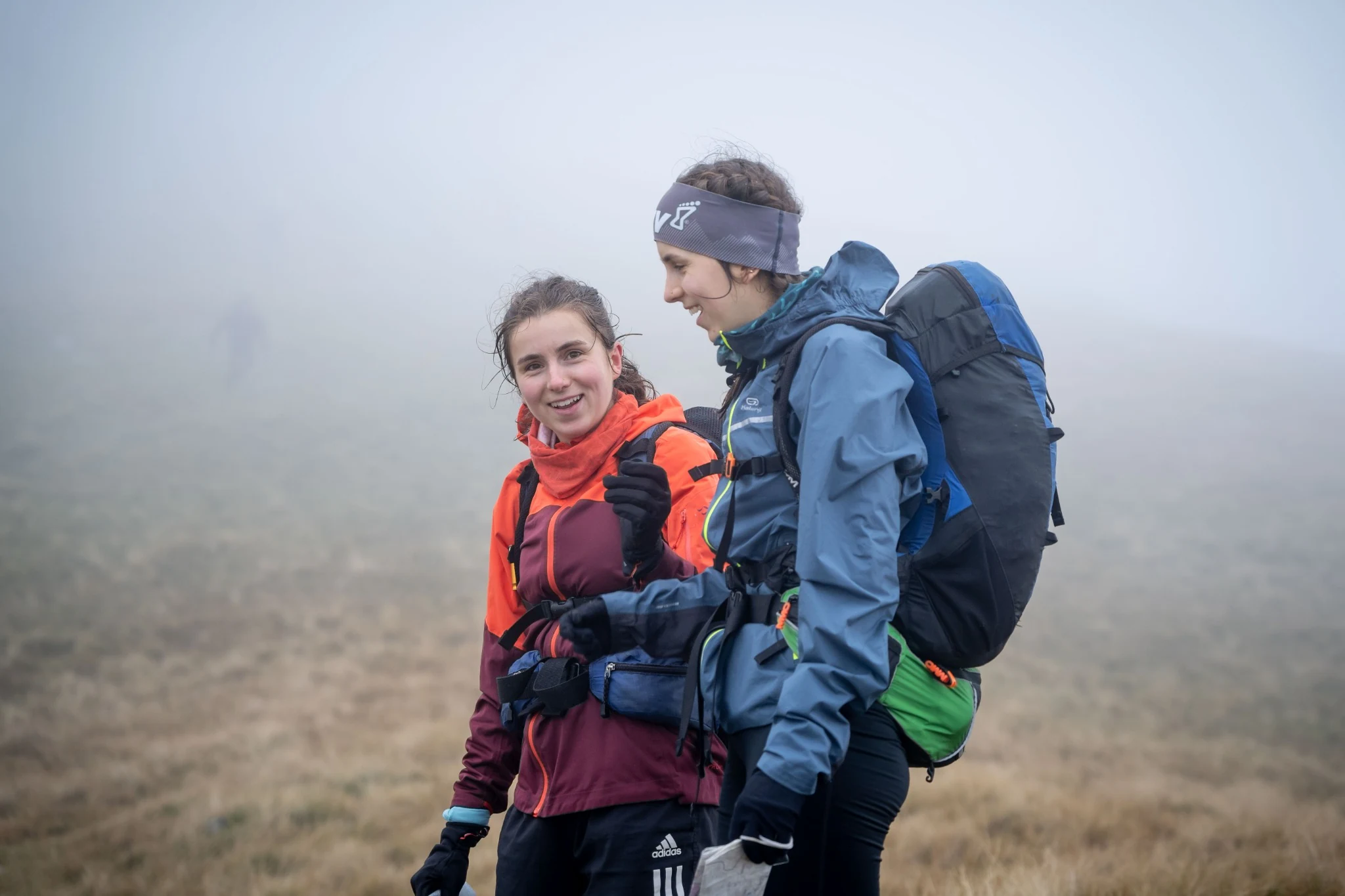 Two OMM competitors in red and blue jackets together on a misty hillside