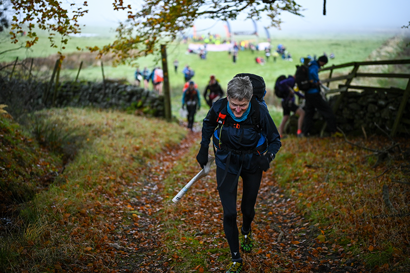 OMM competitor climbing a wooded path with other teams in the background