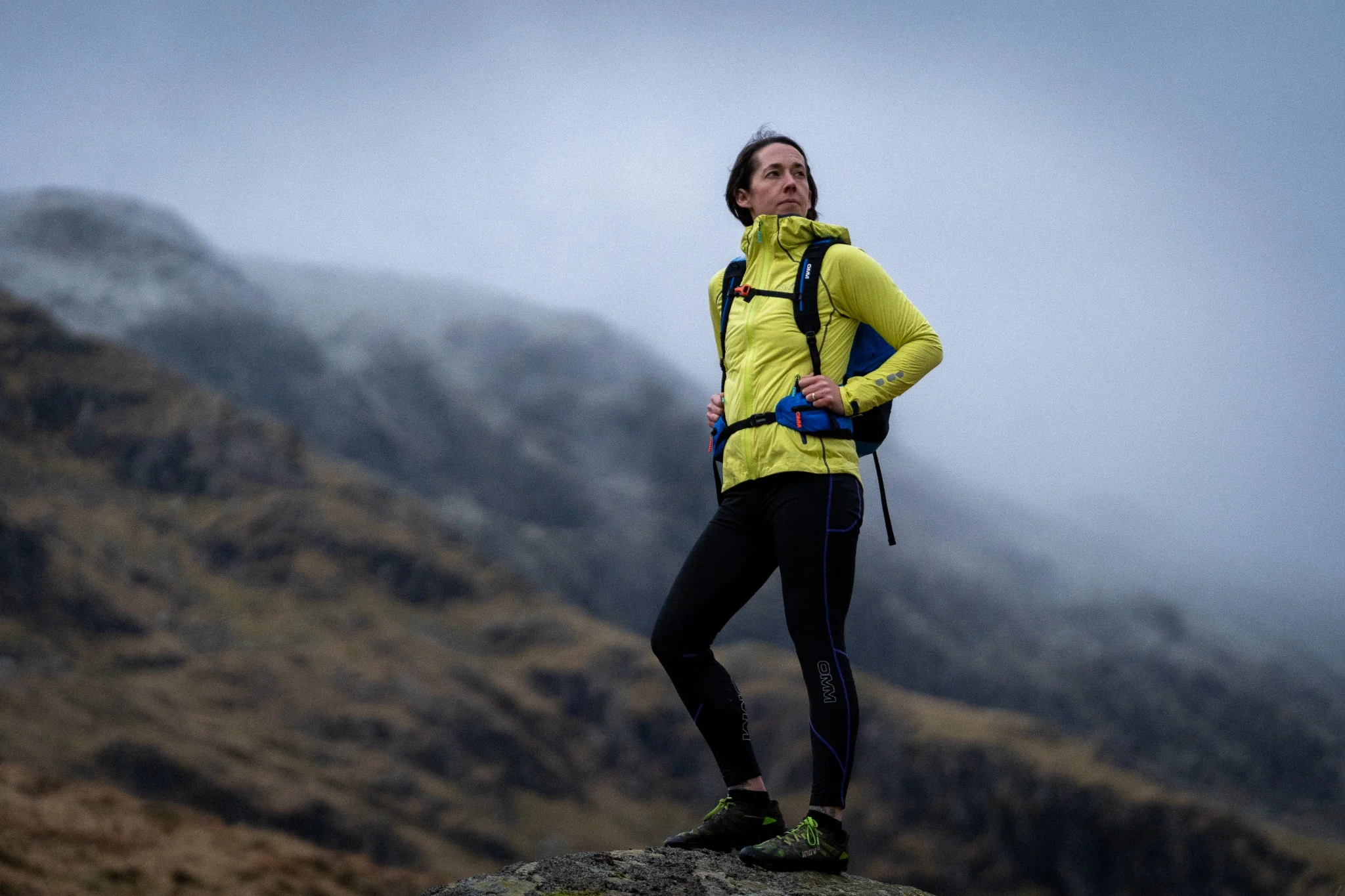OMM runner wearing a yellow shell on a misty mountain.