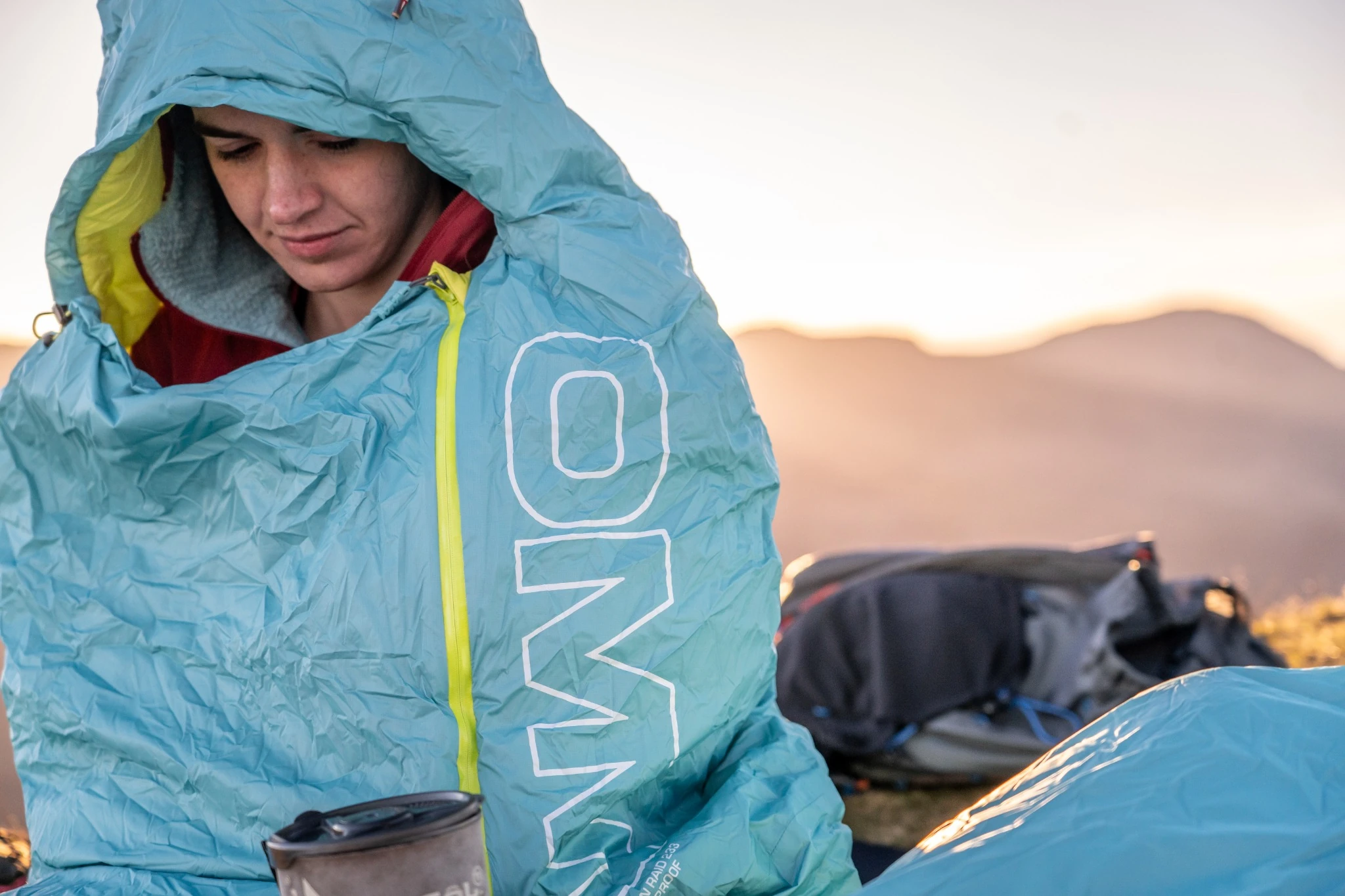 Competitor sitting in a pale blue sleeping bag at camp